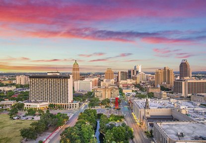 Stunning view of the San Antonio city skyline at sunset, with vibrant pink and purple hues filling the sky above the skyscrapers.