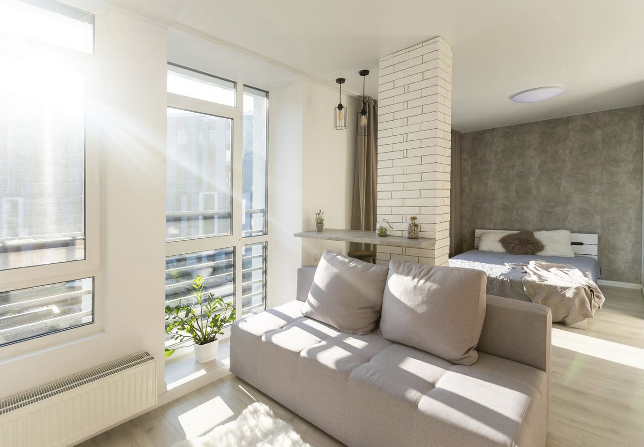 An urban apartment unit with white brick accents and simple decor, featuring city views, a stone wall in the background, and wood panel flooring.