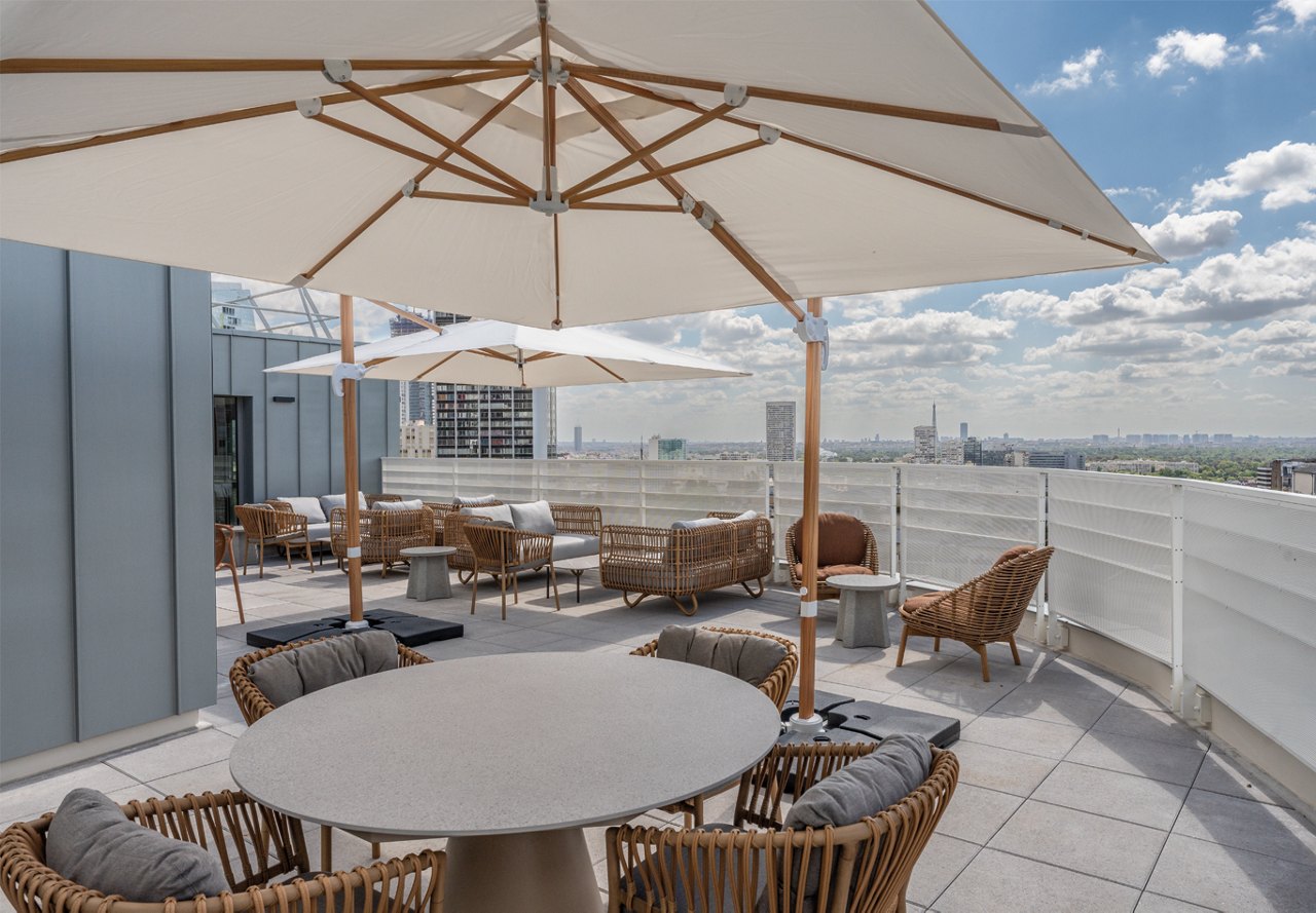 An inviting outdoor rooftop area at an apartment community, featuring stylish tables and umbrellas for residents to relax under the bright blue sky, creating a perfect space for socializing and enjoying the outdoors.