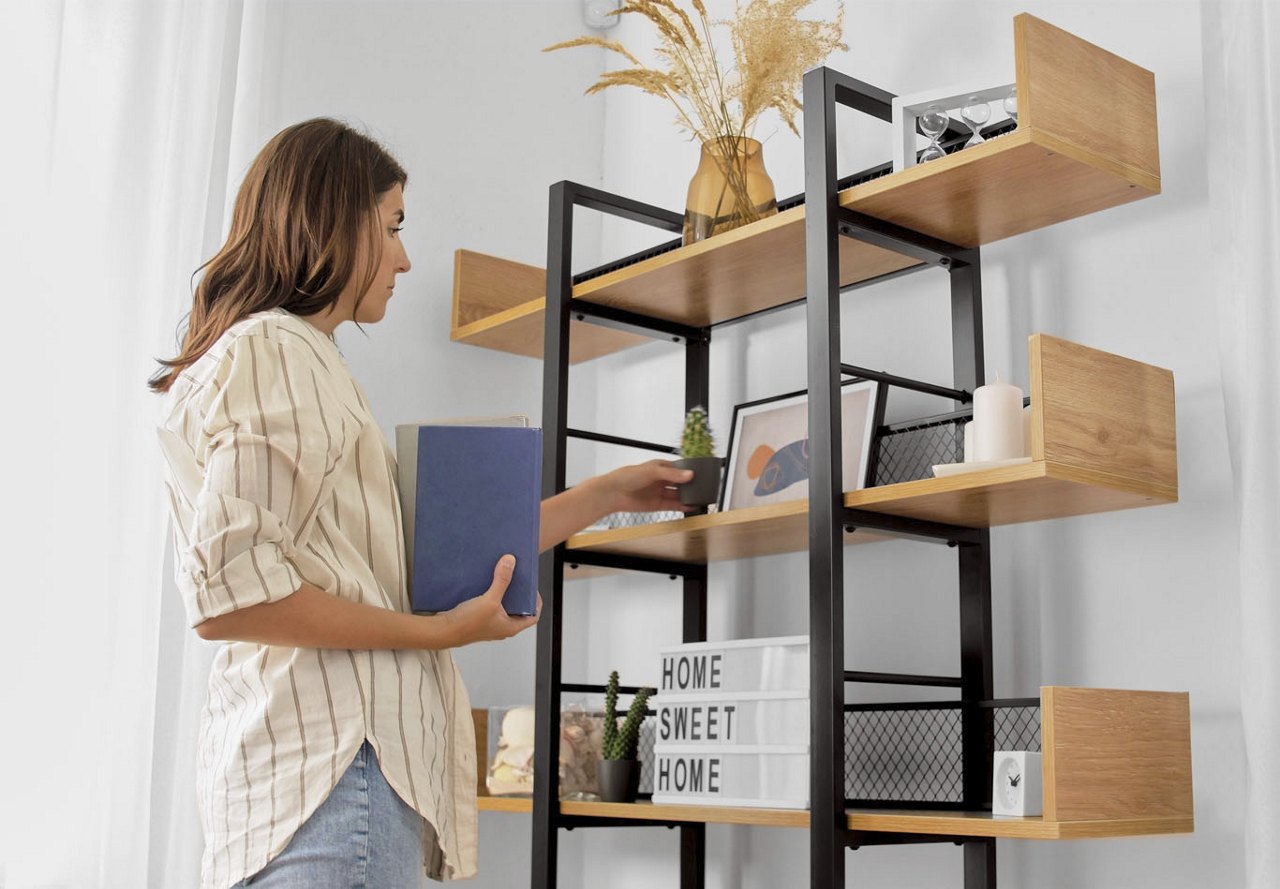 A woman organizing shelves in her new apartment, arranging decor as she adds photos and books to create a personalized and stylish display in her home.