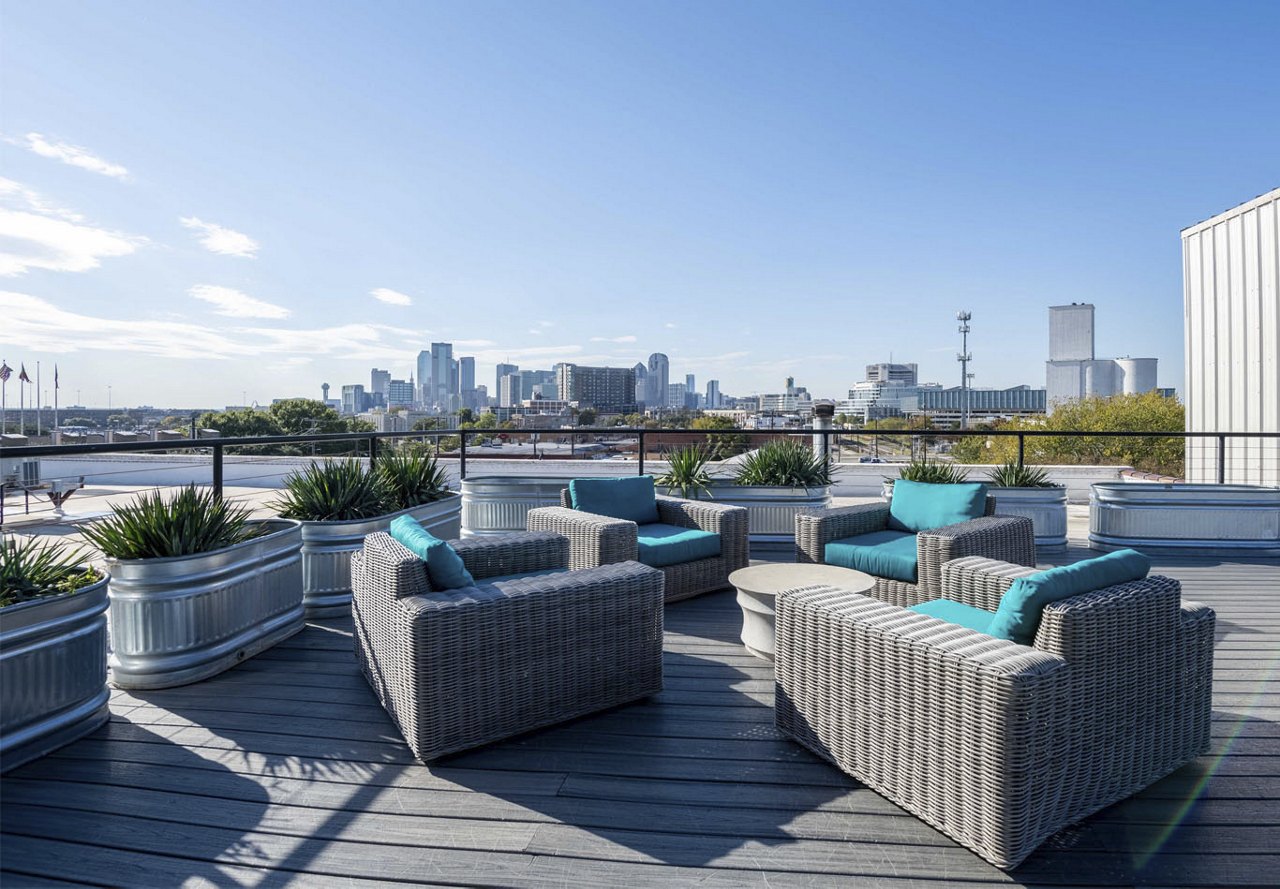 A modern rooftop area in a Dallas apartment community, featuring expansive city views in the background. The space is enhanced with lush greenery, bringing a touch of nature to the stylish outdoor setting.