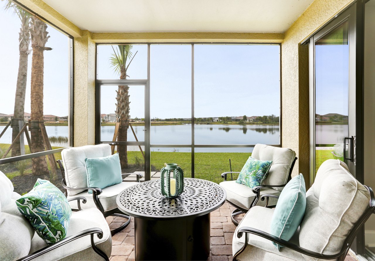 Cozy screened-in porch at a home in Naples, Florida, featuring a water view and palm trees in the lush backyard, with aqua blue accents throughout the decor.