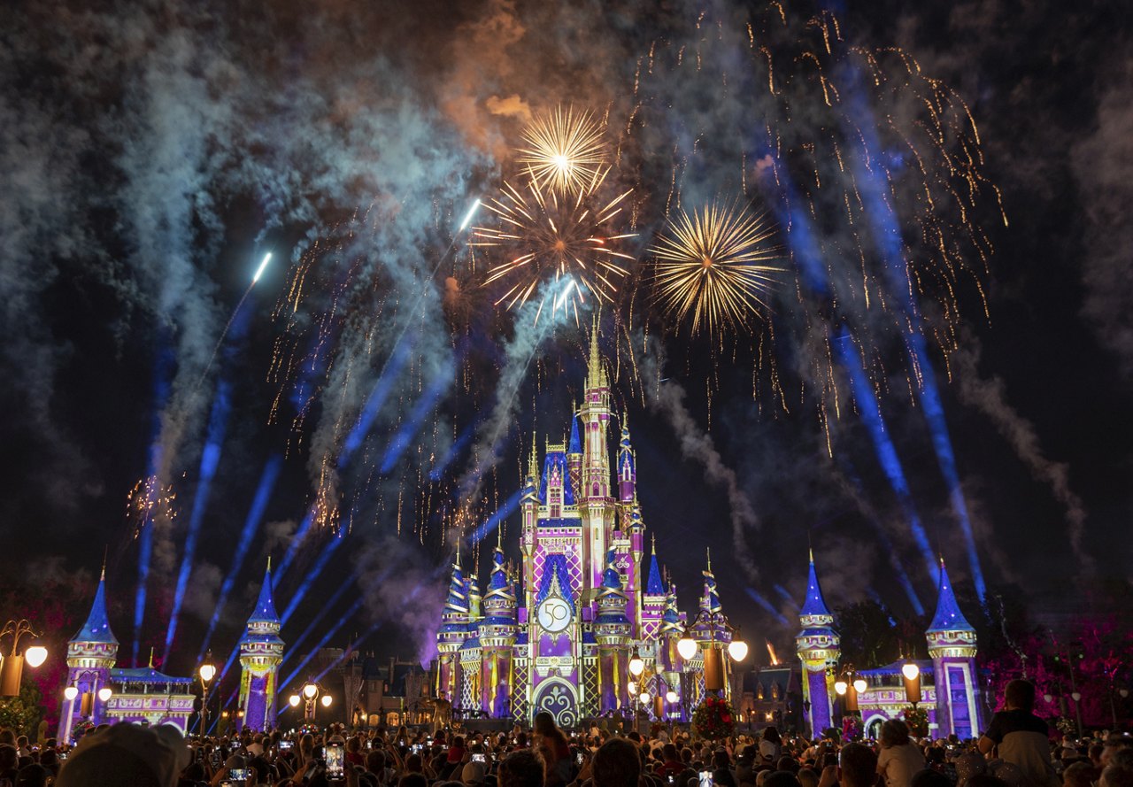 Fireworks display during the nighttime show at Magic Kingdom, Disney World in Orlando, with the castle illuminated in the background and a large crowd watching.