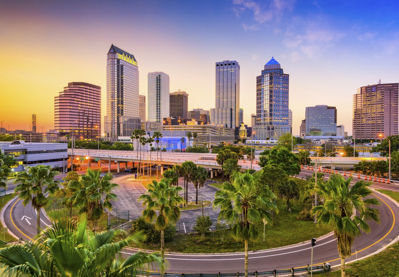 Beautiful view of Tampa with a blue and orange sunset, roads lined with green landscaping, and the cityscape in the background.