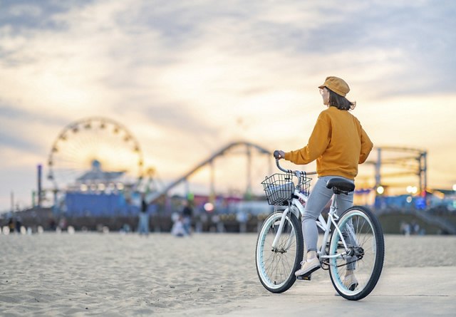 A woman on her bike, gazing at the scenic view of the Santa Monica Pier in the background, enjoying the moment during her ride.