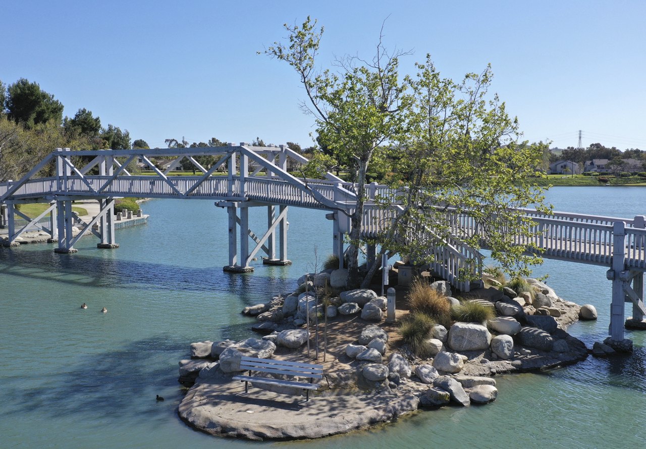 A scenic view of a body of water in Irvine, California, with a bridge crossing over it, surrounded by trees and natural greenery, showcasing the beauty of the area.