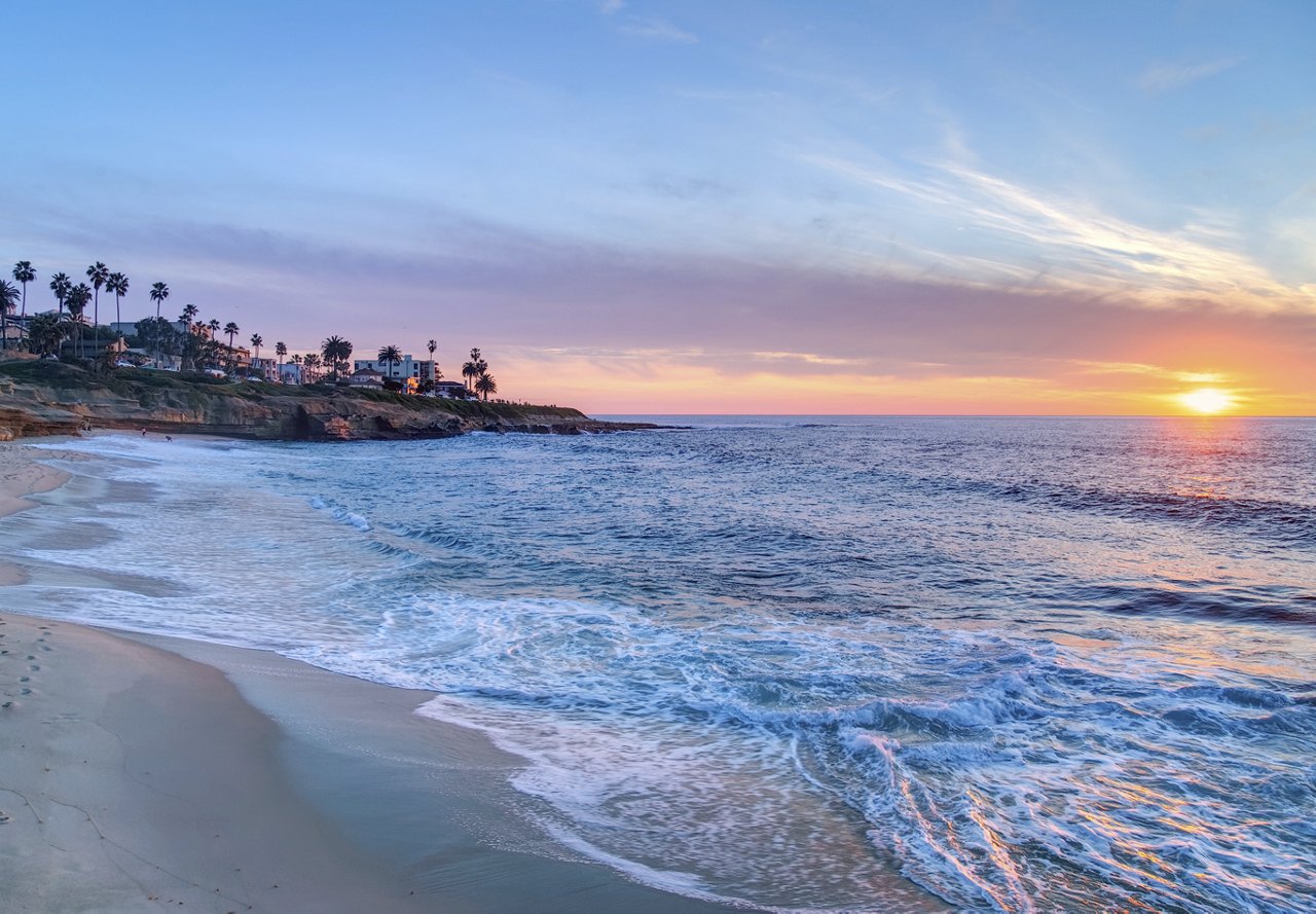 A stunning San Diego beach at sunset, with picturesque waterfront homes and the vibrant natural beauty of the surrounding neighborhood.