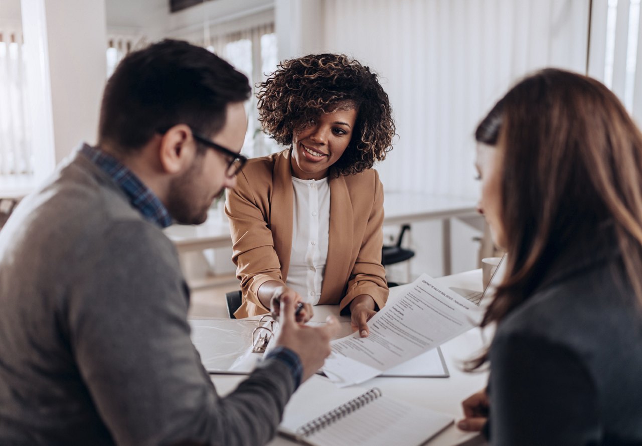 A couple sitting together at the apartment office desk, reviewing their rental paperwork. One person in the couple is acting as a co-signer, while the team member explains the details of the apartment rental process.