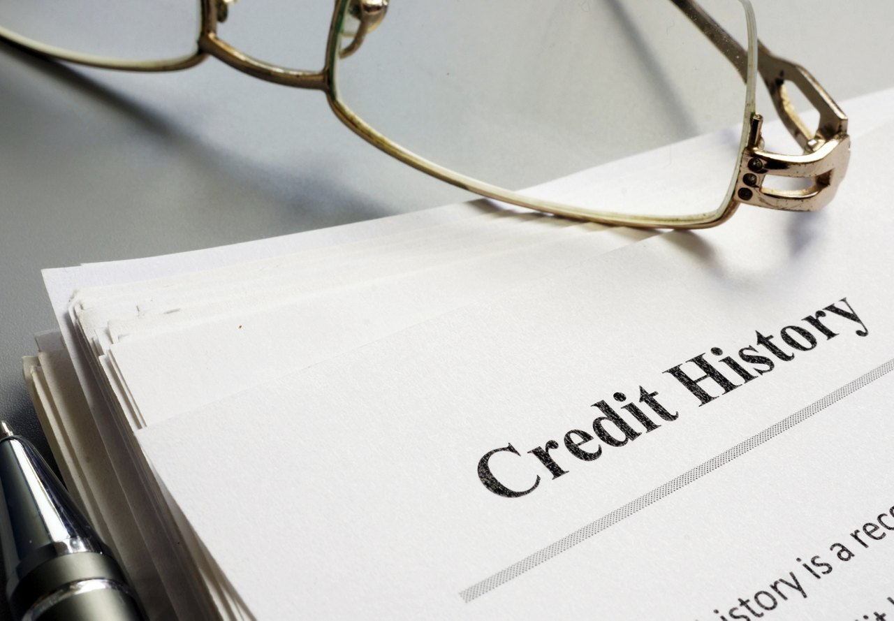 A close-up photo of credit history paperwork with a pair of glasses resting on top, placed on a neutral surface.