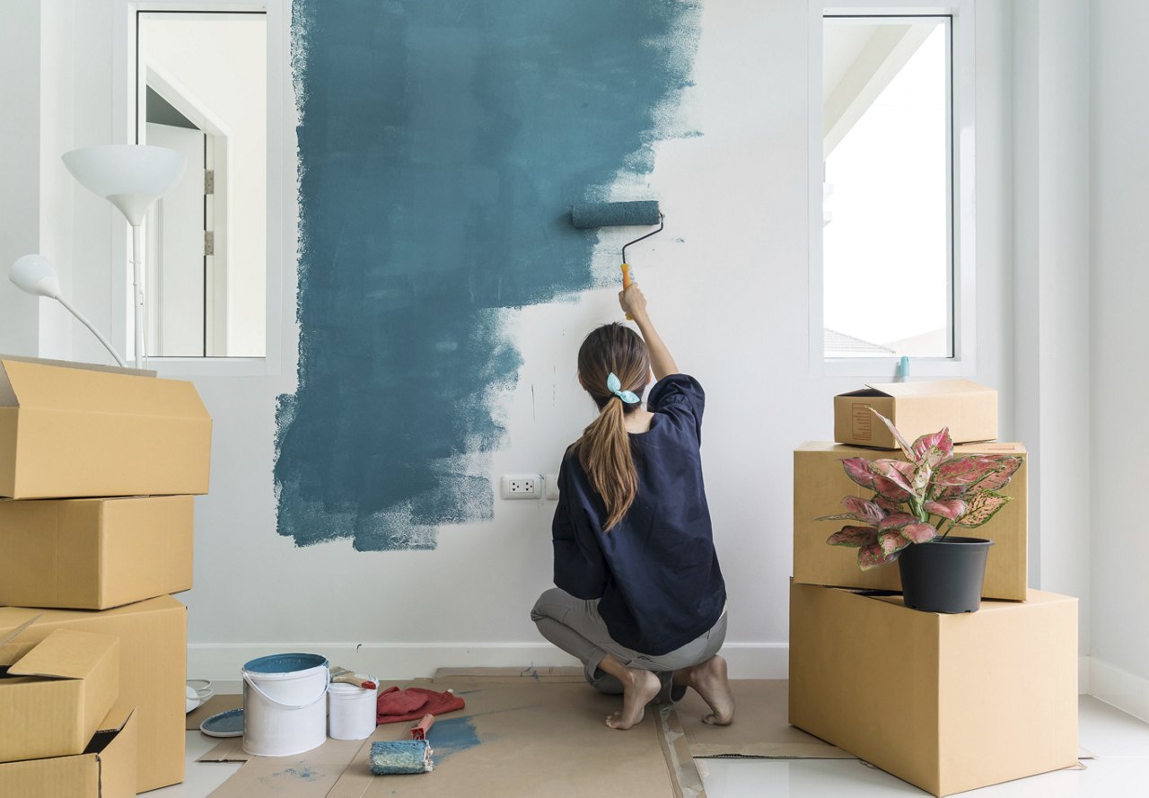 A woman applying blue paint to a wall in her home, surrounded by moving boxes. She’s adding a personal touch to the space as she makes it her own.