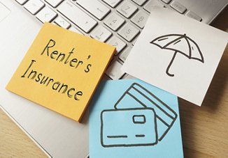 A computer keyboard with sticky notes displaying the words "renters insurance," along with an umbrella and credit cards, symbolizing the topic of renters insurance.