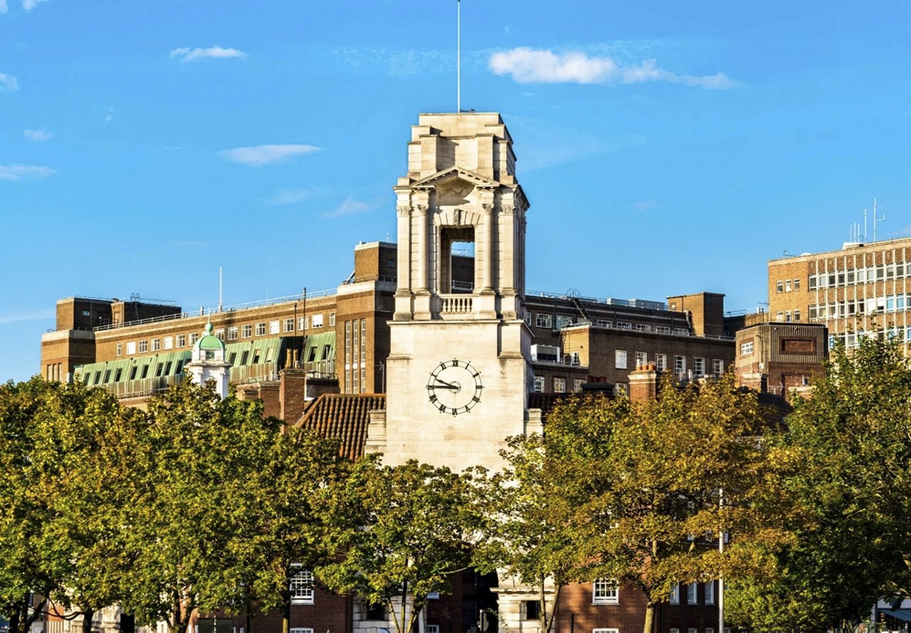 Exterior view of the clocktower on the historic fire station building in the UK, now transformed into student housing, with trees in the foreground and a blue sky above.