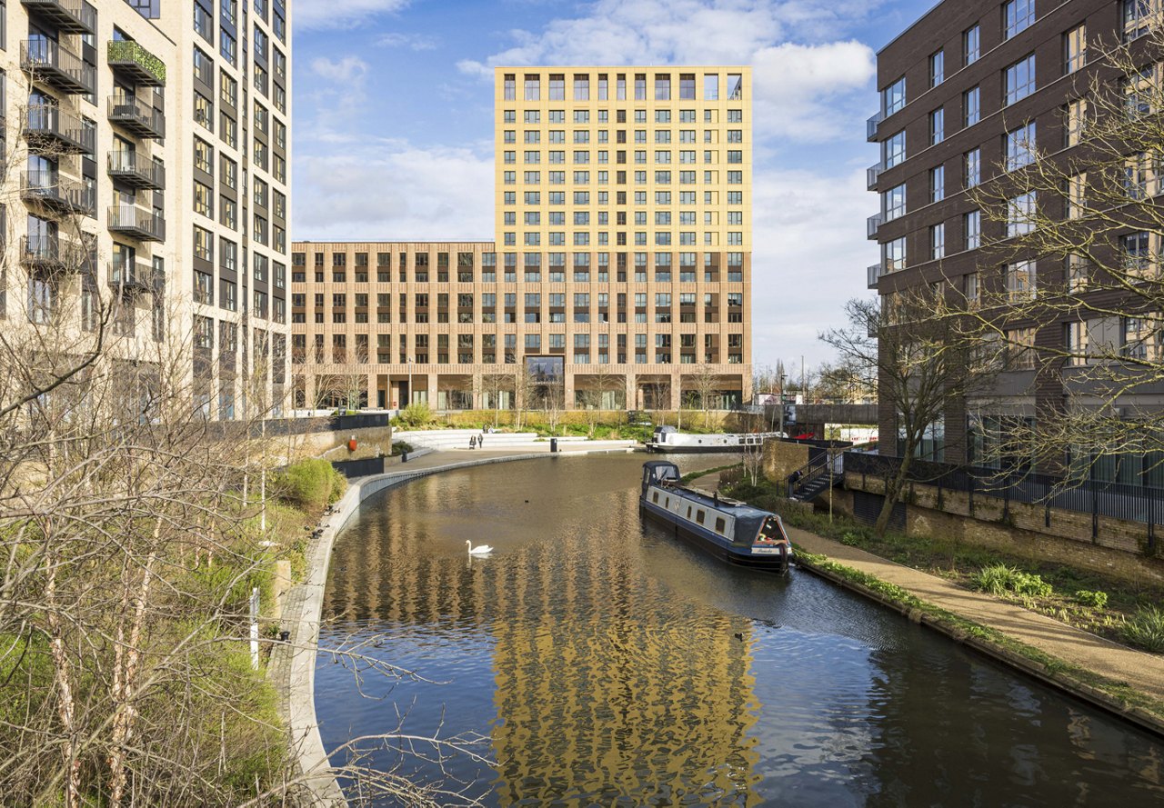 Architectural design of Greenford Quay property in the UK, featuring buildings with water flowing through the center and a clear sky in the background.