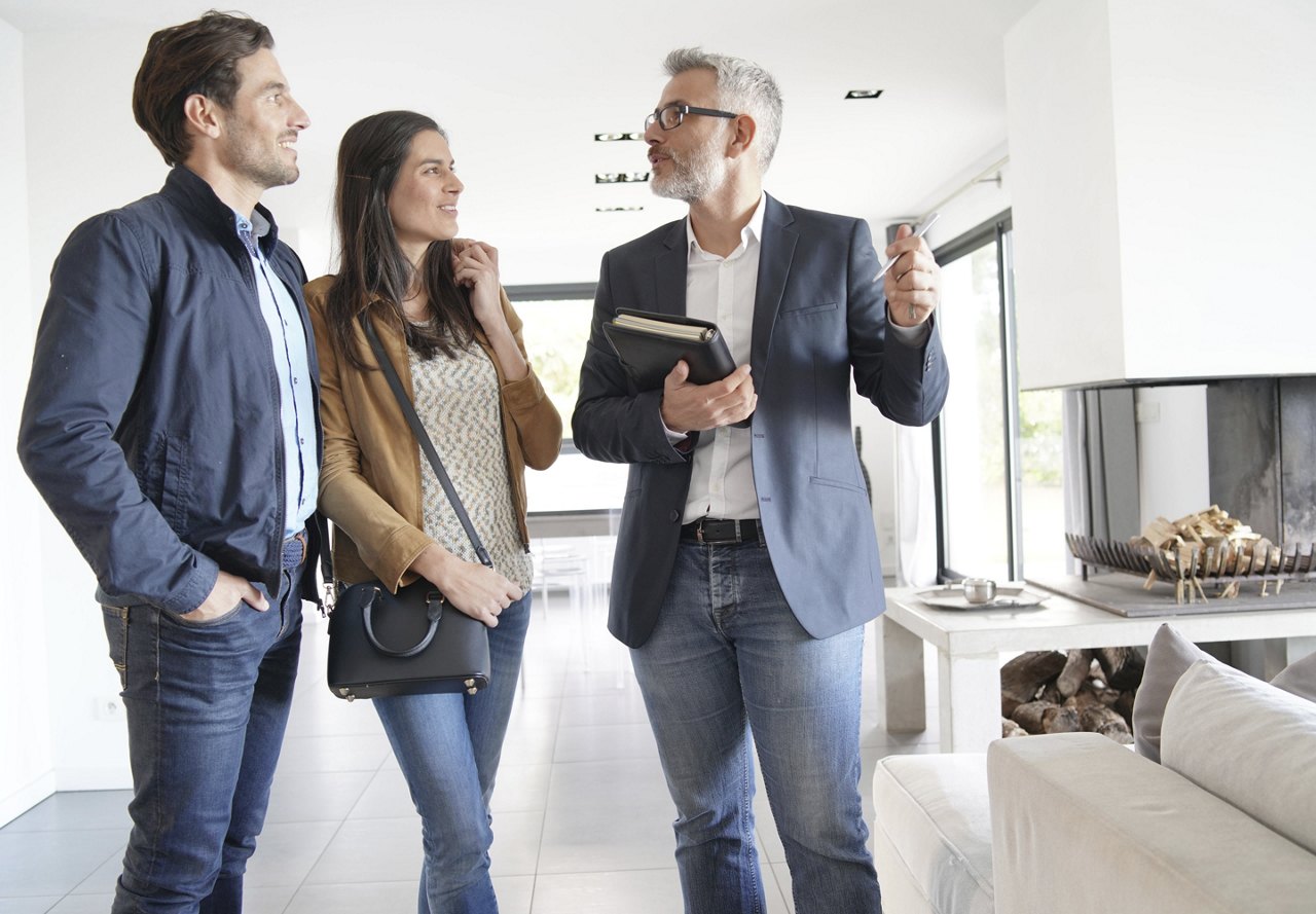 A couple smiling as they tour an apartment with a real estate agent, asking questions as the man looks at the agent while considering their next potential home.