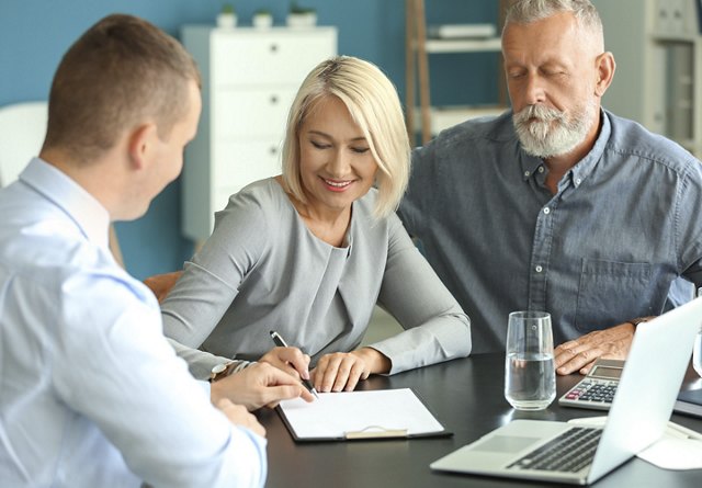 Man and woman signing a lease with a real estate agent for their new home, with various items on the desk and a blurred background.