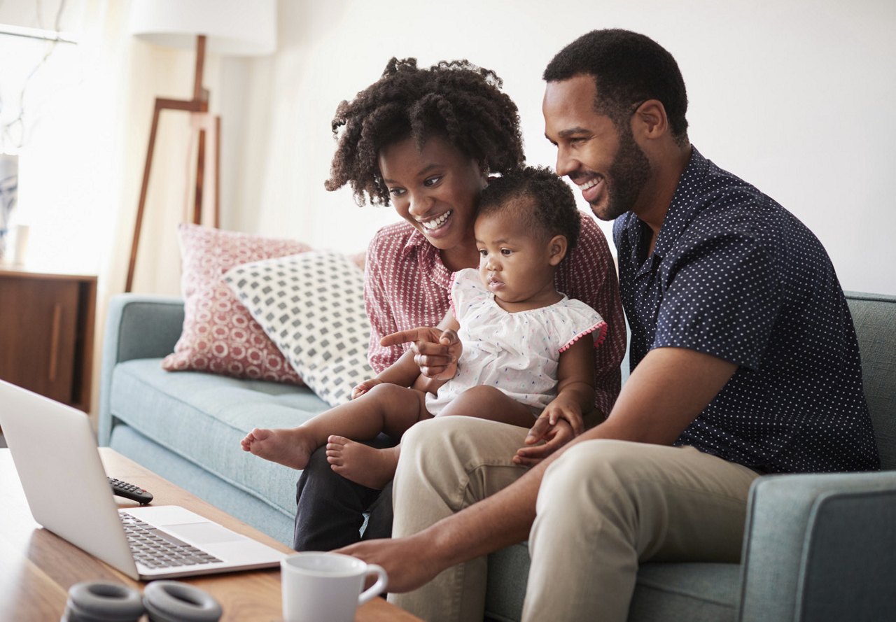 Family sitting together in their living area, looking at a computer while discussing housing options and enjoying their home.