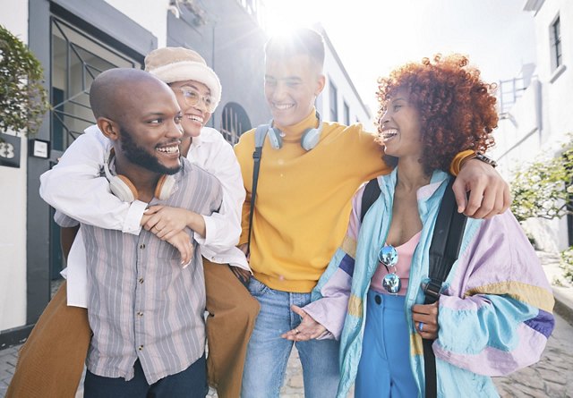 A diverse group of friends walking through a lively college town, carrying backpacks and wearing headphones, smiling and enjoying each other's company.