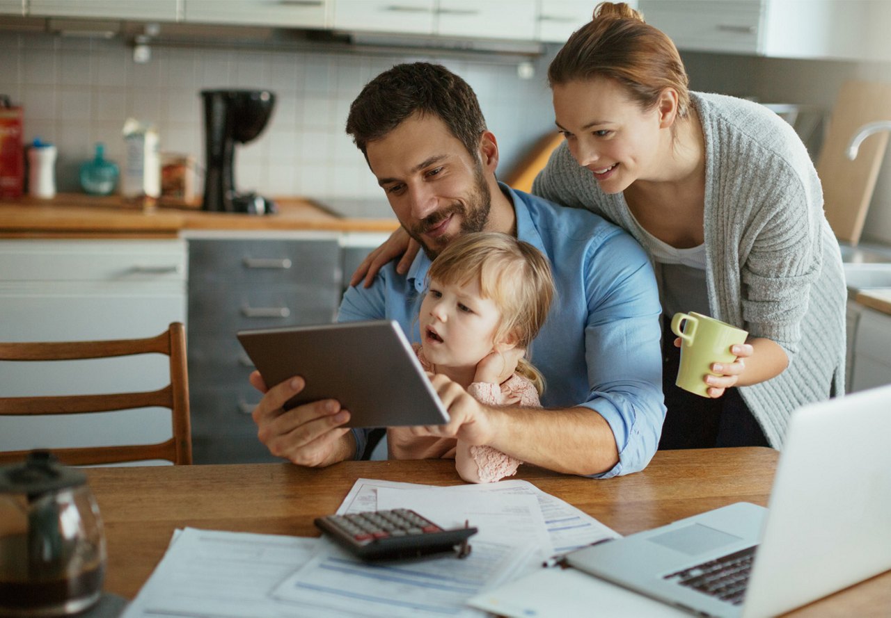 Family budgeting for utilities at the kitchen table, using a tablet, calculator, and paperwork to manage household expenses.