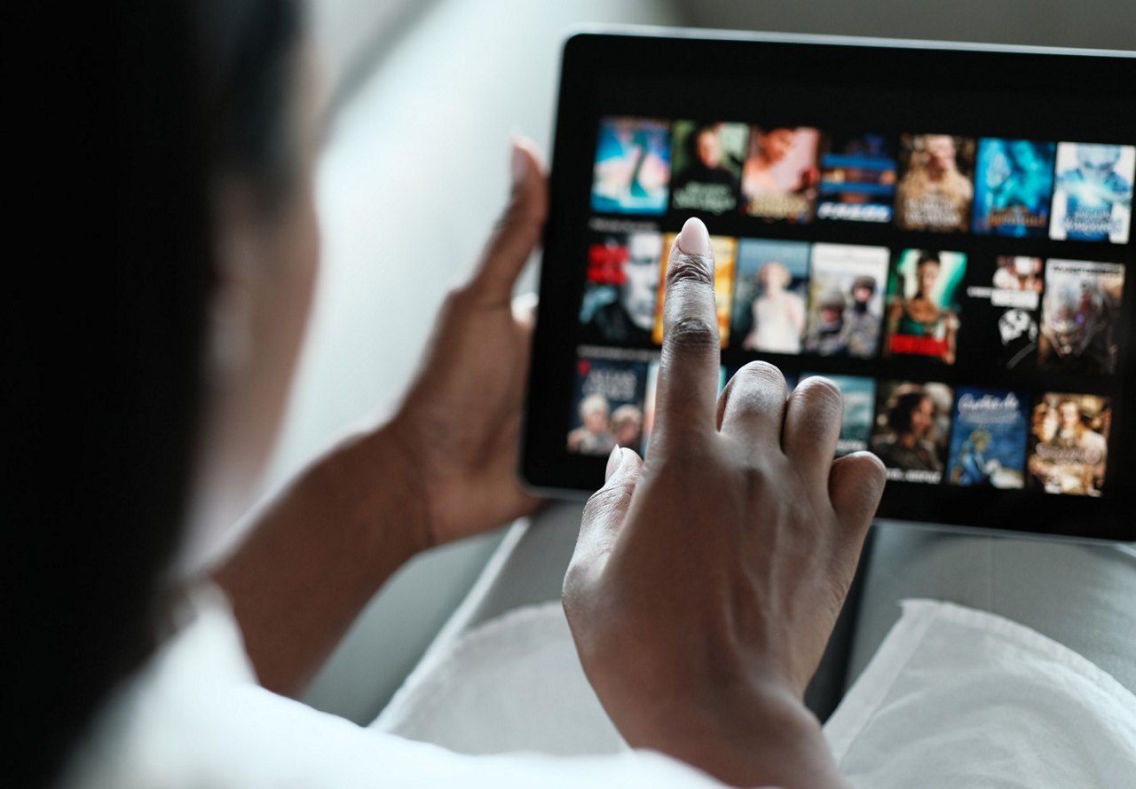 Person relaxing on the couch, scrolling through a streaming service on their iPad to choose what to watch in their living room.