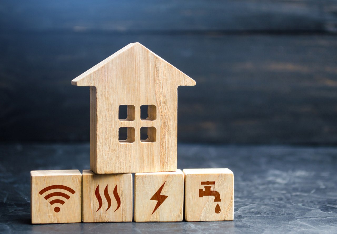 Wooden blocks on blue marble, each highlighting different icons to represent utilities, with a wooden house block placed on top.