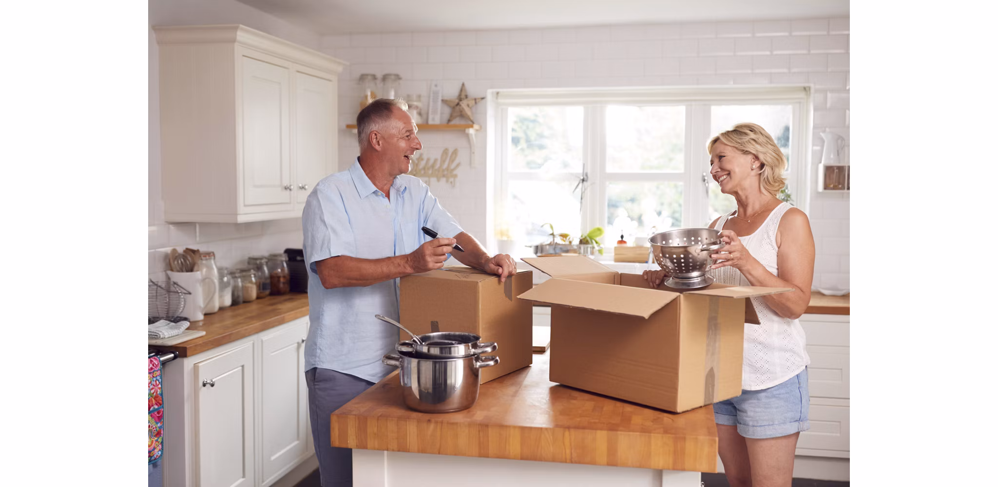 Smiling man and woman packing boxes in their kitchen as they prepare to downsize and move into a smaller space.