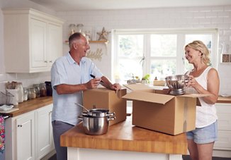 Smiling man and woman packing boxes in their kitchen as they prepare to downsize and move into a smaller space.