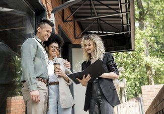 People chatting with an apartment rental team member, smiling as they look at a folder she is holding, while searching for their new home together.