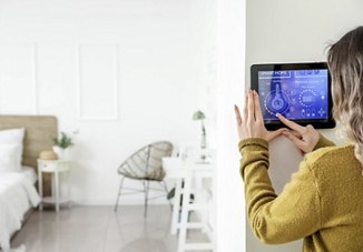 Woman using a digital panel in her home to adjust the smart thermostat, with a softly blurred view of her bedroom in the background.