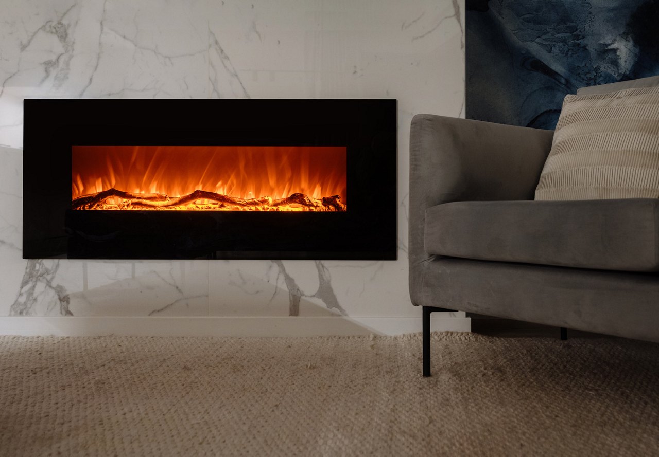 A view of a cozy living area featuring a modern fireplace, complemented by a relaxing chair and a carpeted area in front, creating a warm and inviting space to unwind during the winter months.