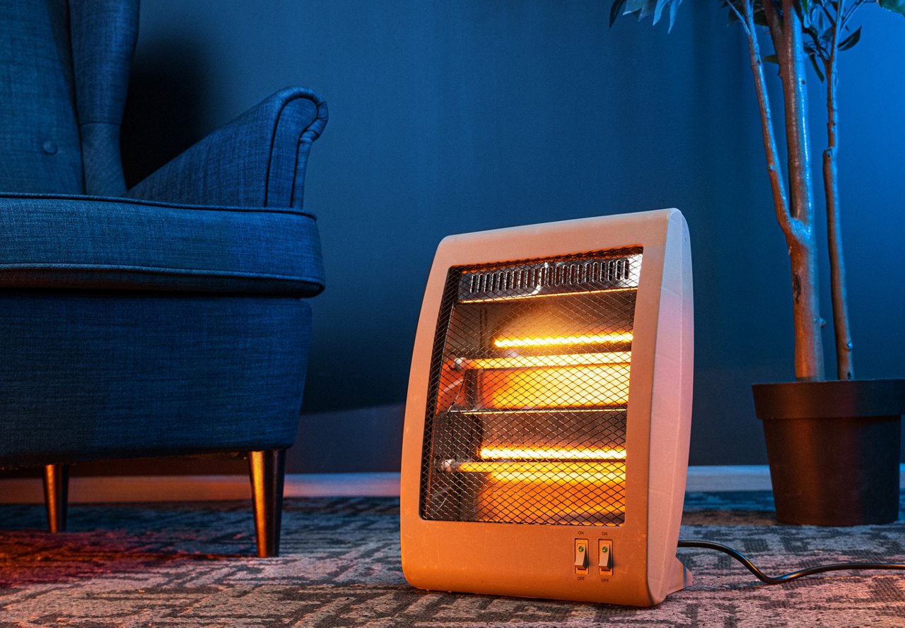 A close-up view of a space heater in a room, warming the space, with a chair and a small potted tree adding a decorative touch to the cozy setting.