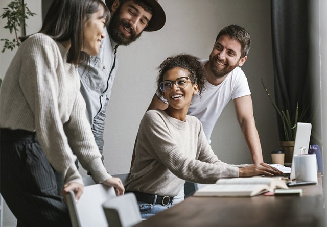 A group of young professionals collaborating in a casual office space, engaging in discussion with minimal decor and simple touches around them.