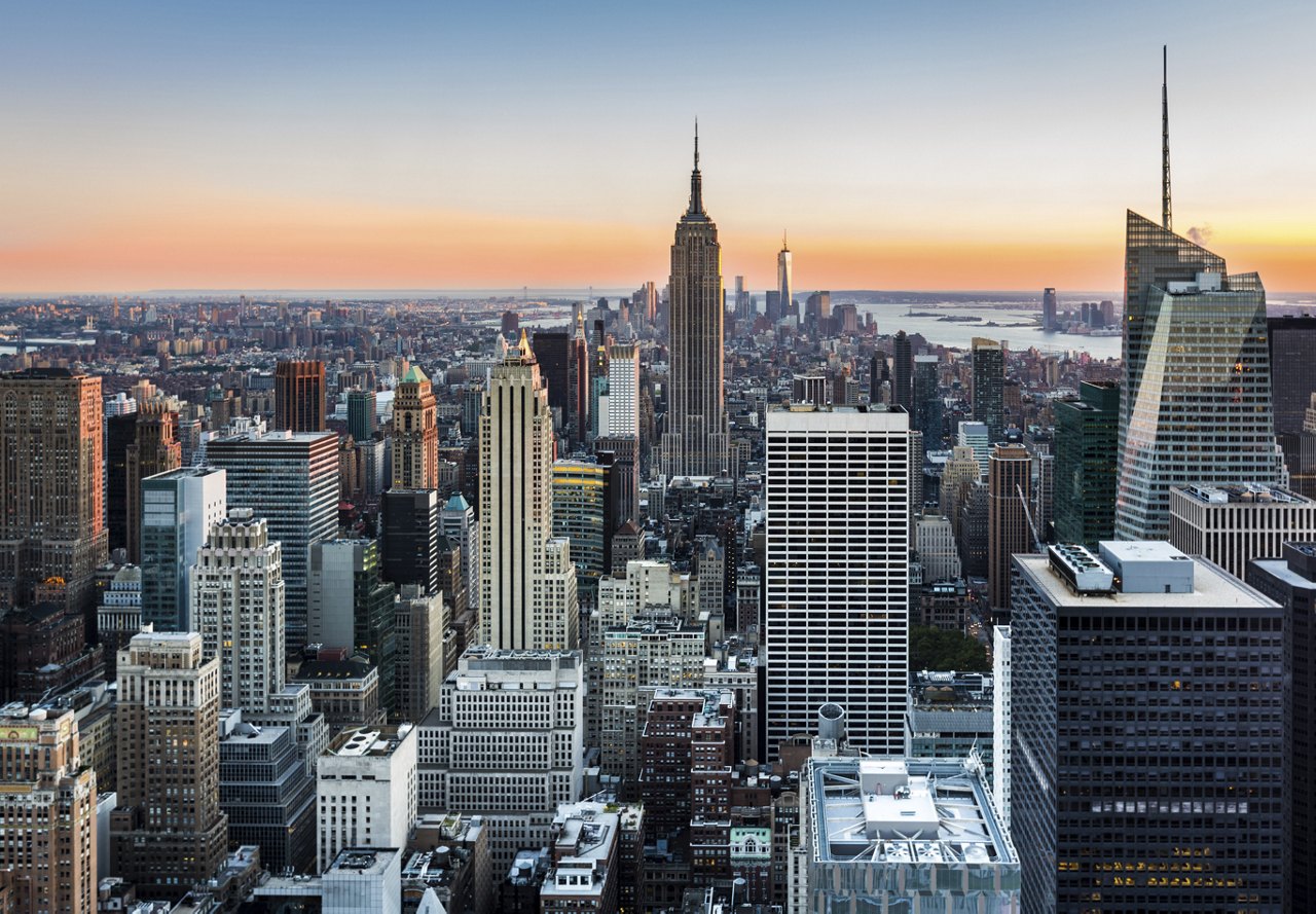 A breathtaking view of Manhattan, New York City, at sunset, with the Hudson River reflecting the warm hues of the sky.