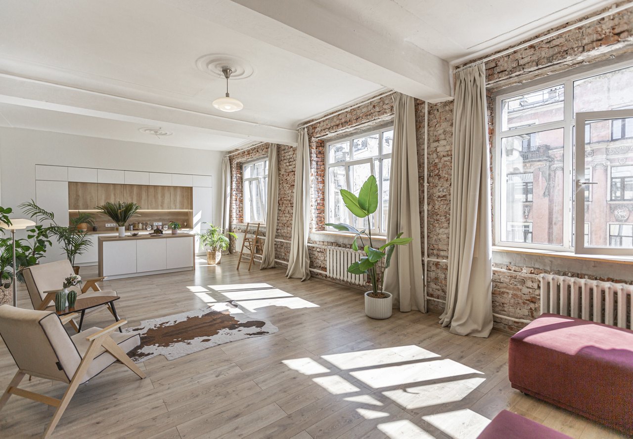 An open floor plan of an apartment featuring exposed brick, modern finishes, and an abundance of natural light flooding the space.