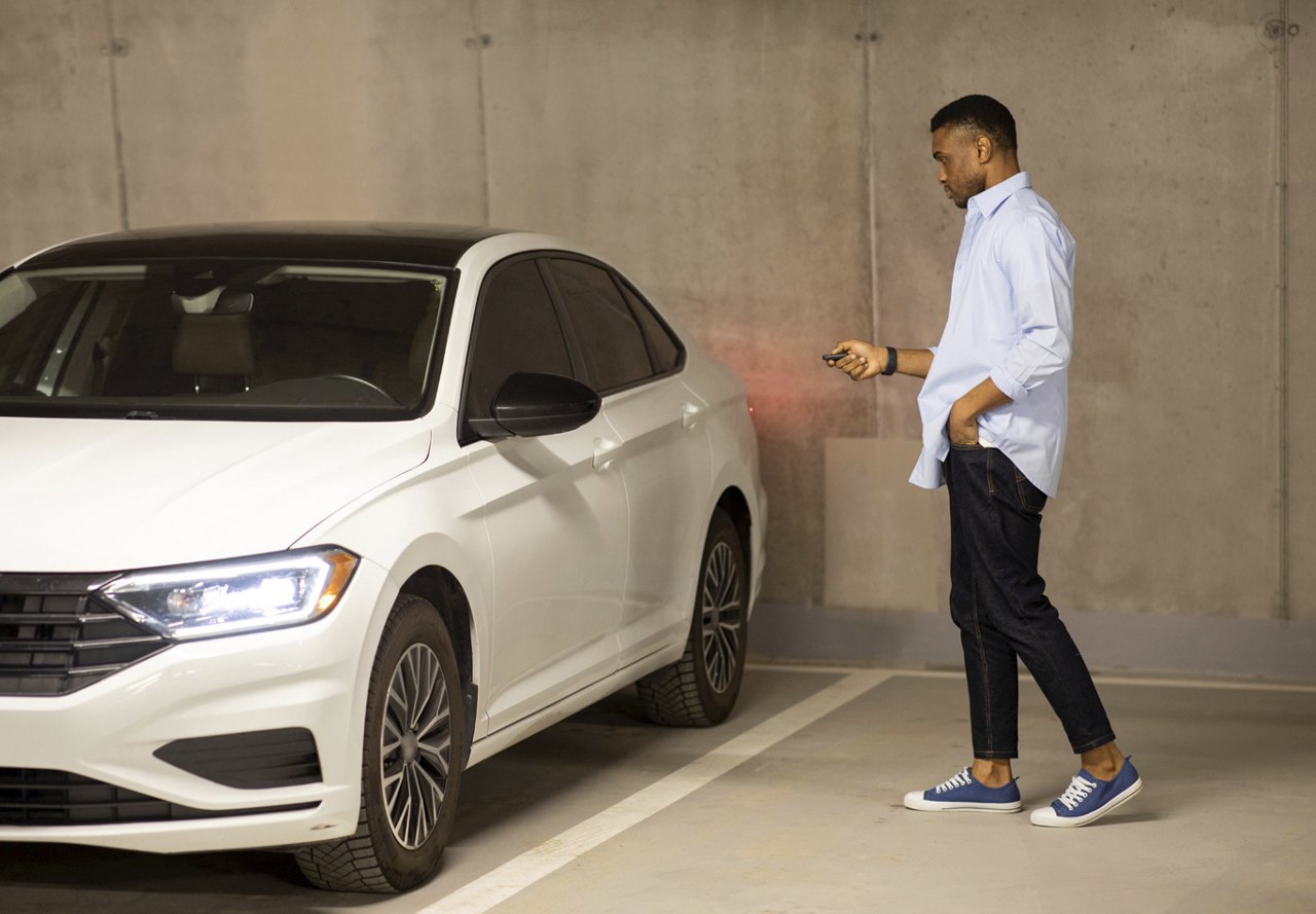 A man walks toward his parked car in a dimly lit parking garage. As he approaches, the tail lights illuminate, signaling that the vehicle has been unlocked and is ready to be driven.