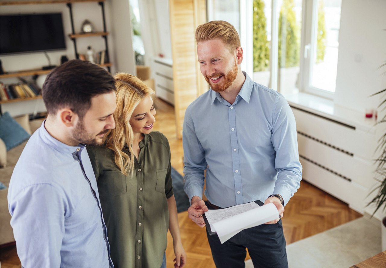 A couple discusses details with apartment staff during a tour of an apartment unit, with one person holding a paper to share specific information, while the apartment's interior is visible in the background.