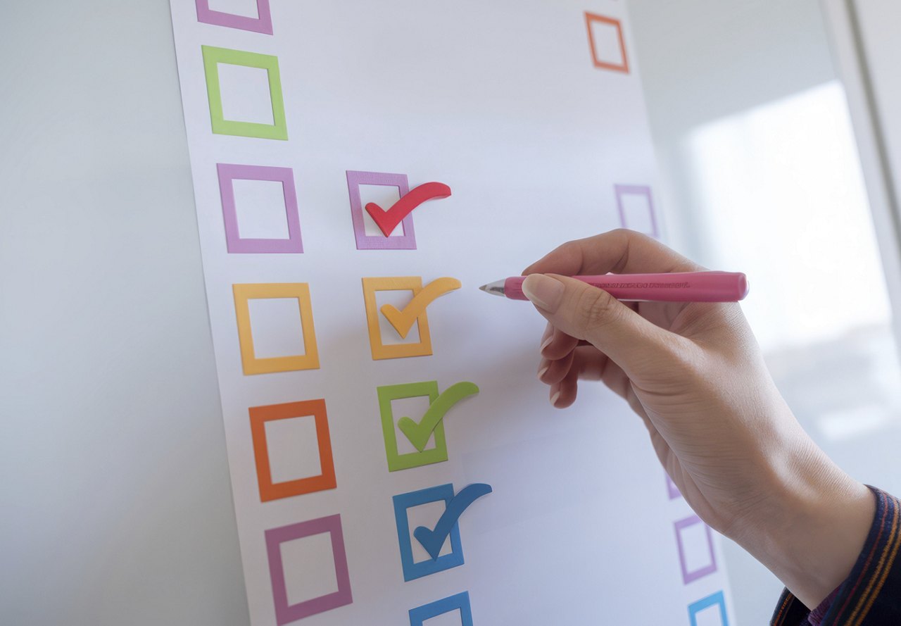 A person writing on a colorful checklist, using a pink pen to check off completed tasks.