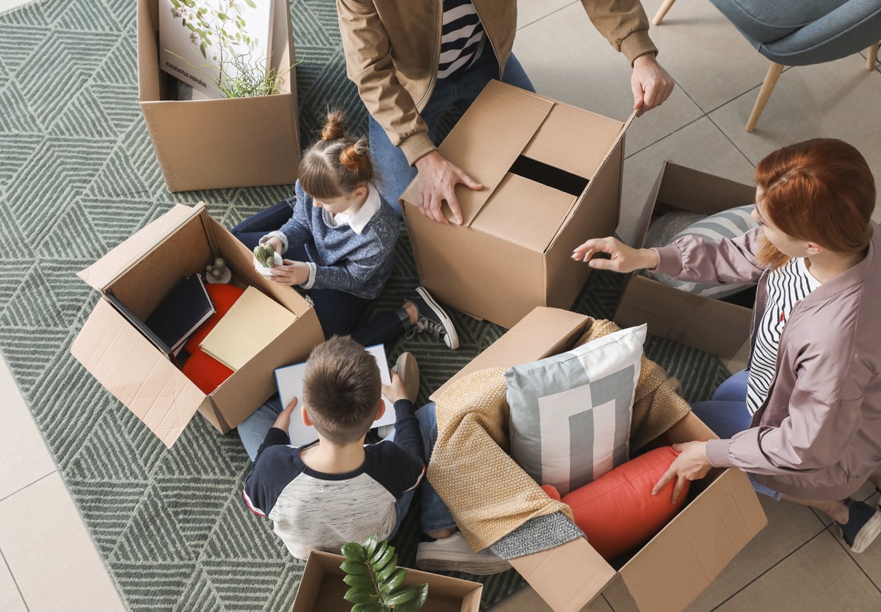 A family with parents and kids packing their belongings into cardboard boxes, preparing for their move, with a clear view of the items being organized.