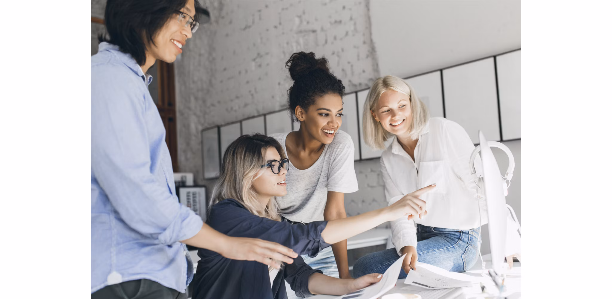 Group of young professionals collaborating and smiling around a computer.