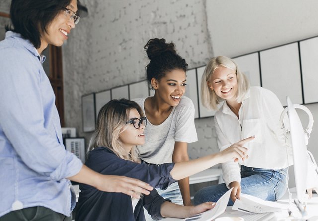 Group of young professionals collaborating and smiling around a computer.