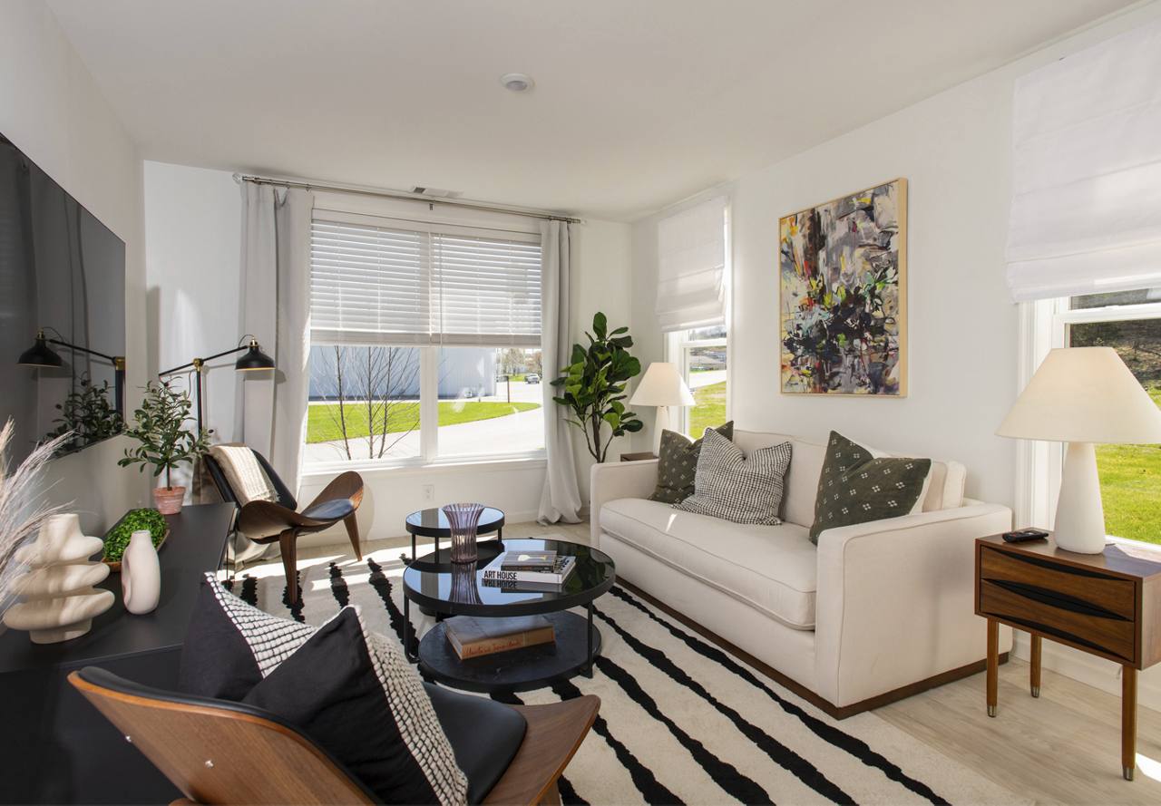 Brightly lit living room with modern decor, featuring a white sofa, wooden furniture, and an abstract painting on the wall.