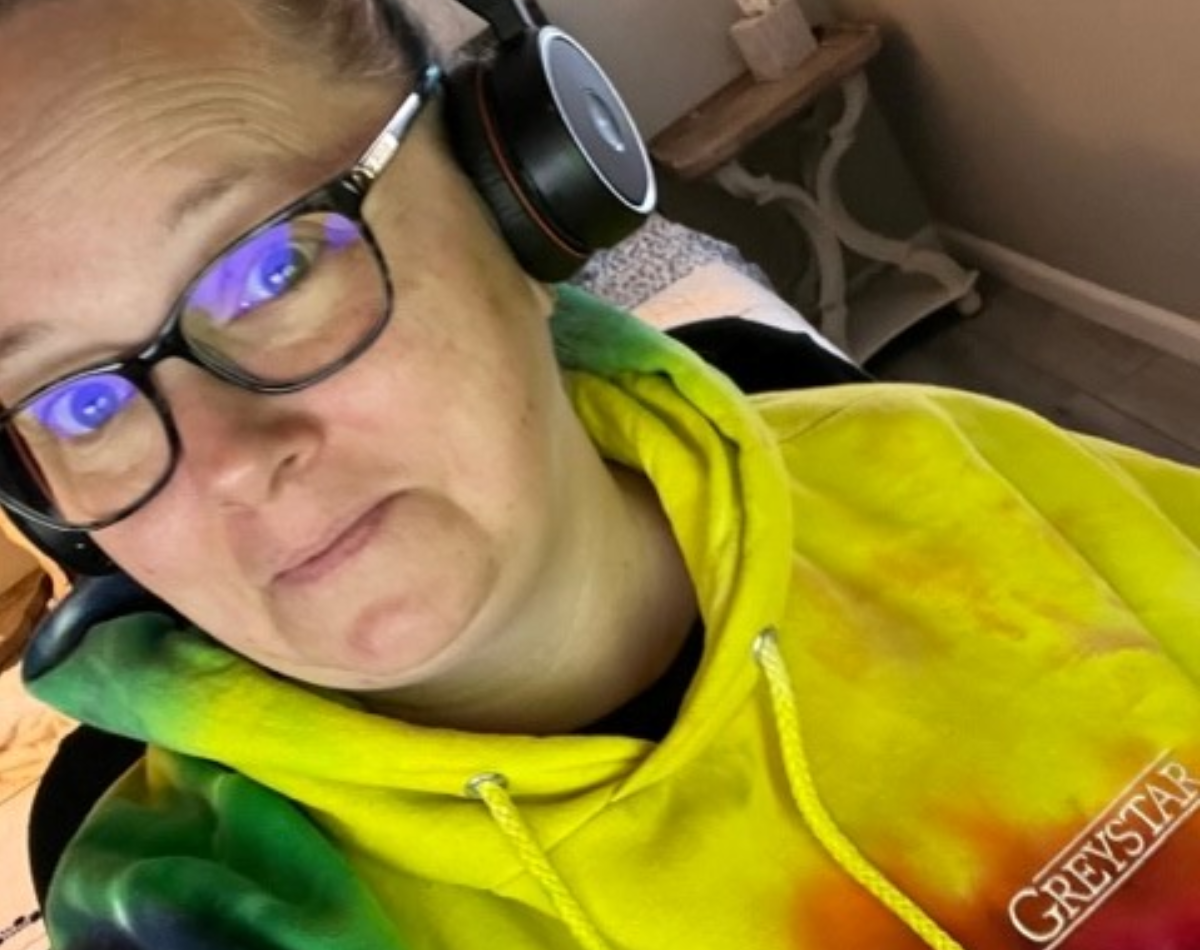 Individual wearing a tie-dye hoodie with 'GREYSTAR' branding and headphones, giving a subtle smile to the camera.