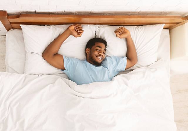 smiling man in bed stretching his arms
