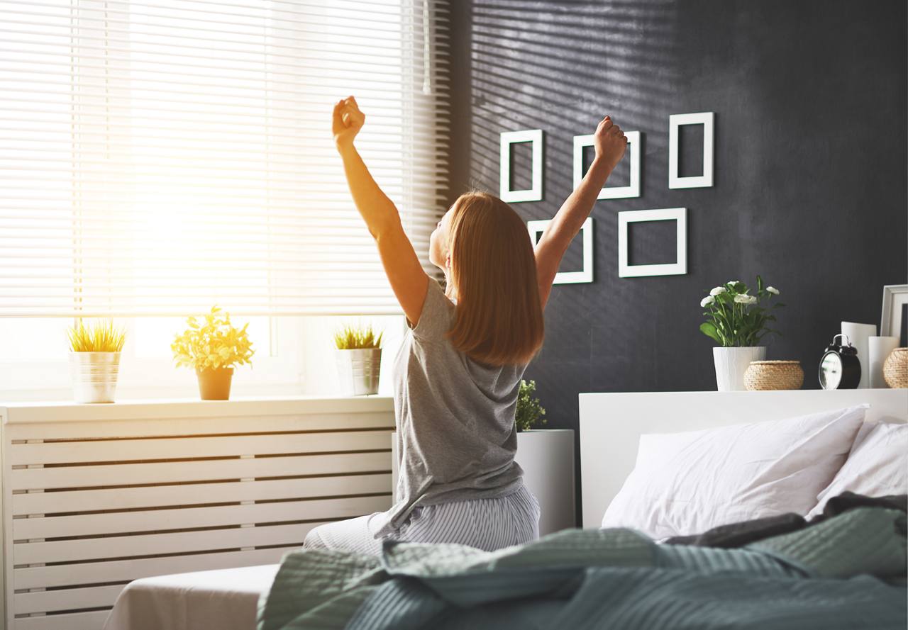 woman sitting on bed stretching arms above her head