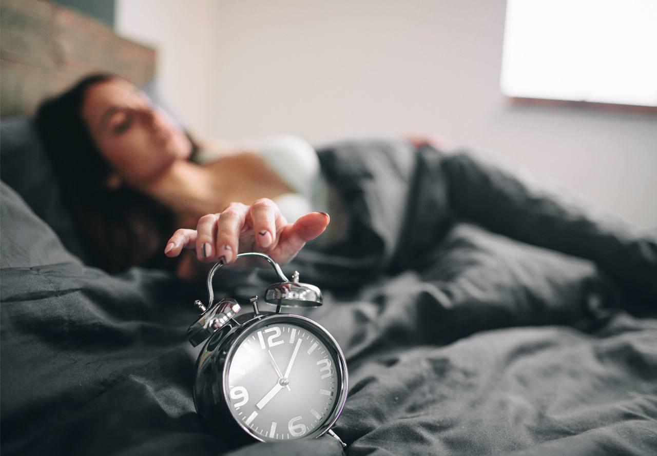 woman hitting alarm clock snooze button