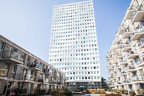 Contemporary architecture with a striking white high-rise building contrasting with multi-story residential units, set against a clear blue sky.