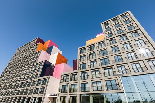 Modern buildings with a mix of traditional and avant-garde designs, featuring colorful geometric shapes on top under a bright blue sky.