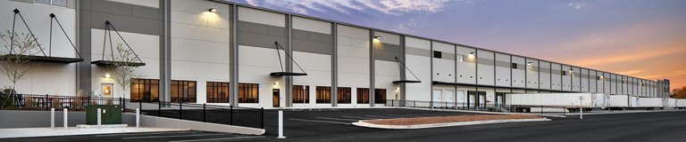 Exterior view of a large industrial warehouse with multiple loading docks and a parking lot, captured at dusk.