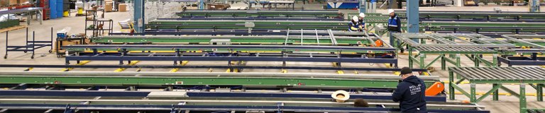 An expansive interior of an industrial facility with a network of conveyor belts and workers overseeing operations, illuminated by bright overhead lighting.