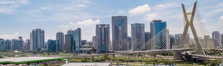 Urban skyline featuring the Estaiada Bridge and modern skyscrapers in São Paulo, Brazil, under a blue sky with clouds.