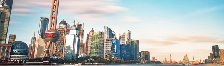 Panoramic view of the Shanghai Bund, showcasing a vibrant skyline with a mix of historic colonial buildings along the waterfront and modern skyscrapers in the background, under a clear sky.